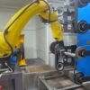 Robotic polishing fixture holding a metal part near a finishing wheel