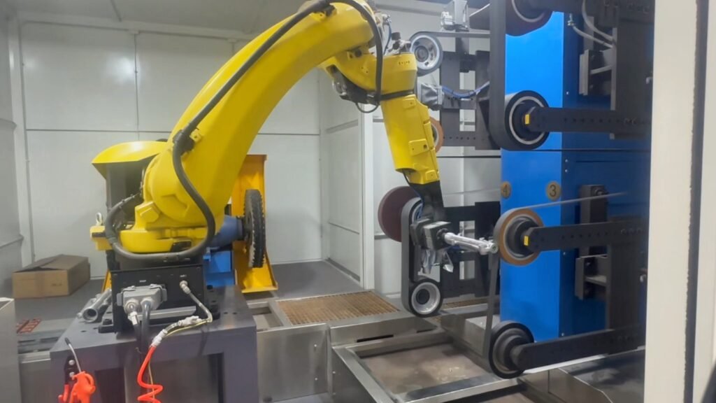 Robotic polishing fixture holding a metal part near a finishing wheel