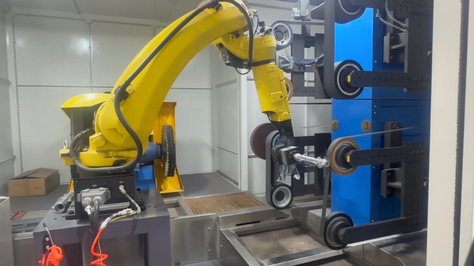 Robotic polishing fixture holding a metal part near a finishing wheel
